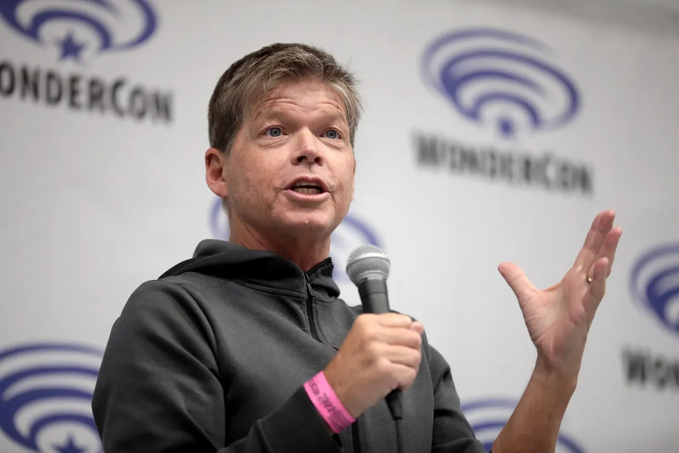 Rob Liefeld speaking on stage at a comic convention, holding a microphone